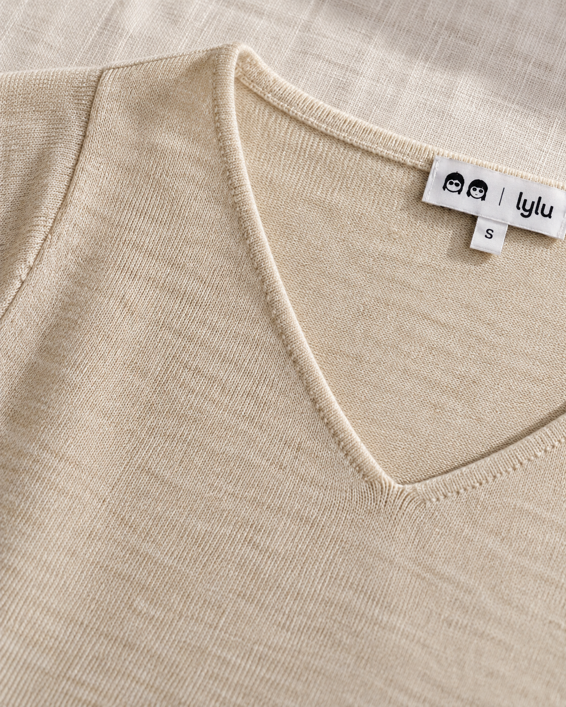 Detalle del cuello de pico, el remate y la textura de punto fino del jersey beige Besalú de LYLU.