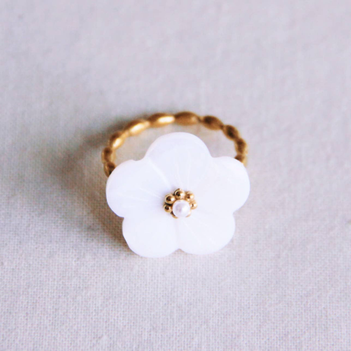 Anillo Liria de acero dorado con aro retorcido y flor blanca nacarada