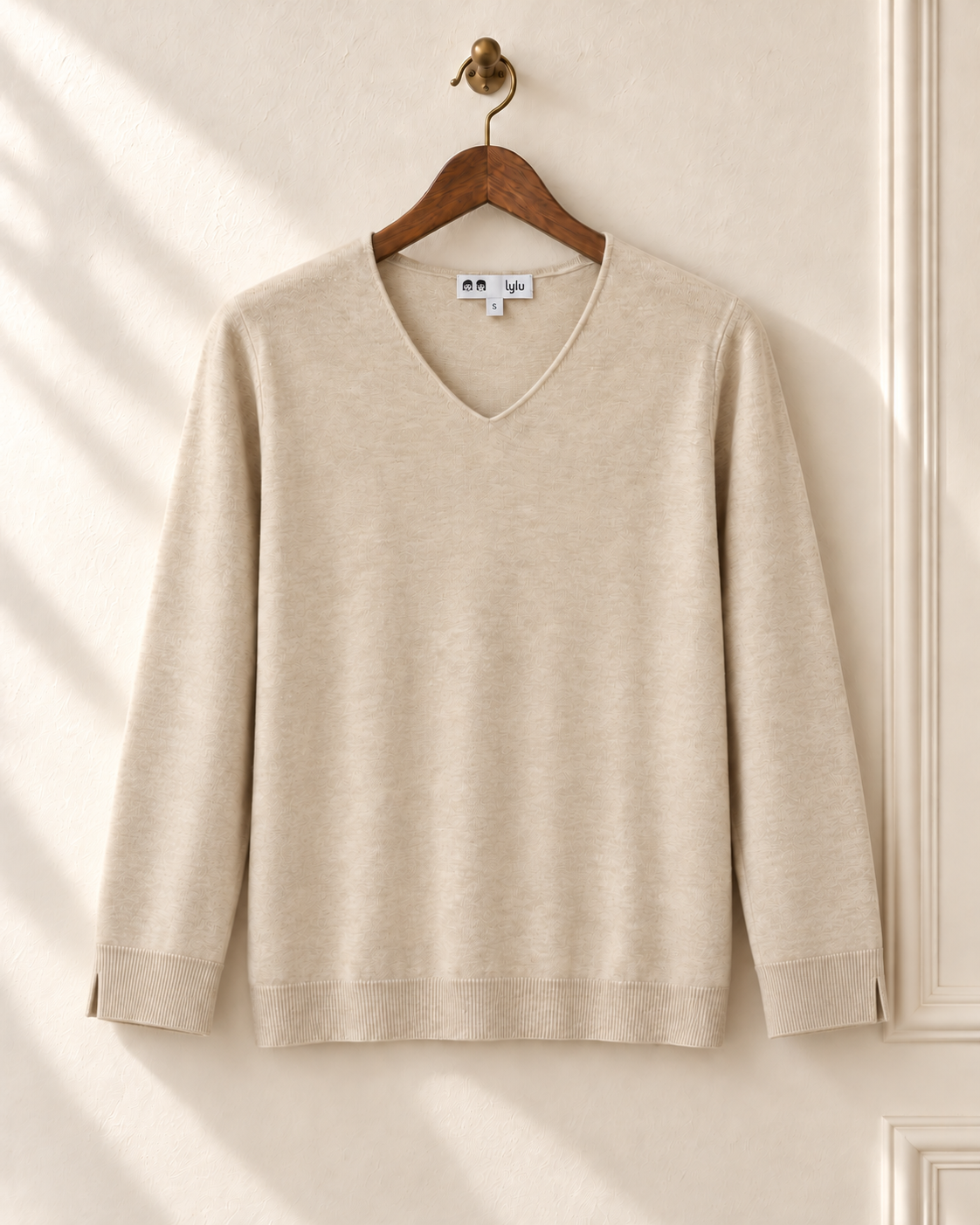 Jersey fino beige Besalú de LYLU en percha, con cuello de pico y una pequeña abertura exterior en cada puño.