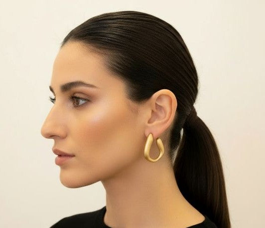 modelo luciendo pendientes dorados mate de aro irregular con acabado elegante y contemporáneo
